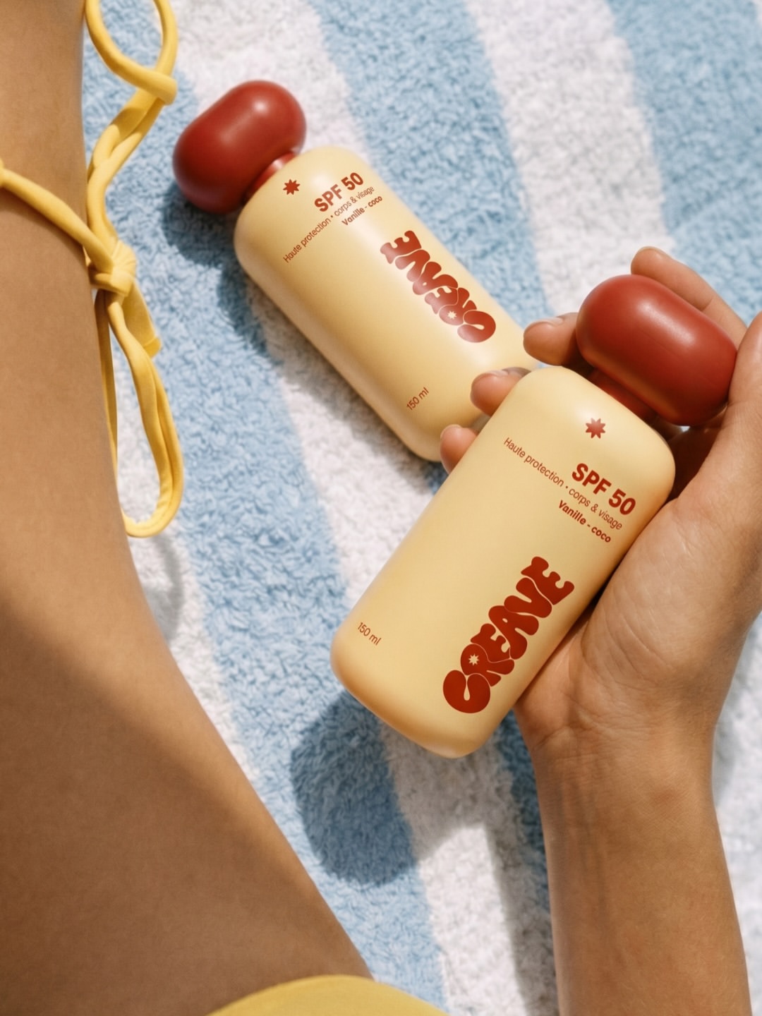Deux flacons CREAVE SPF 50 tenus au-dessus d'une serviette rayée bleue