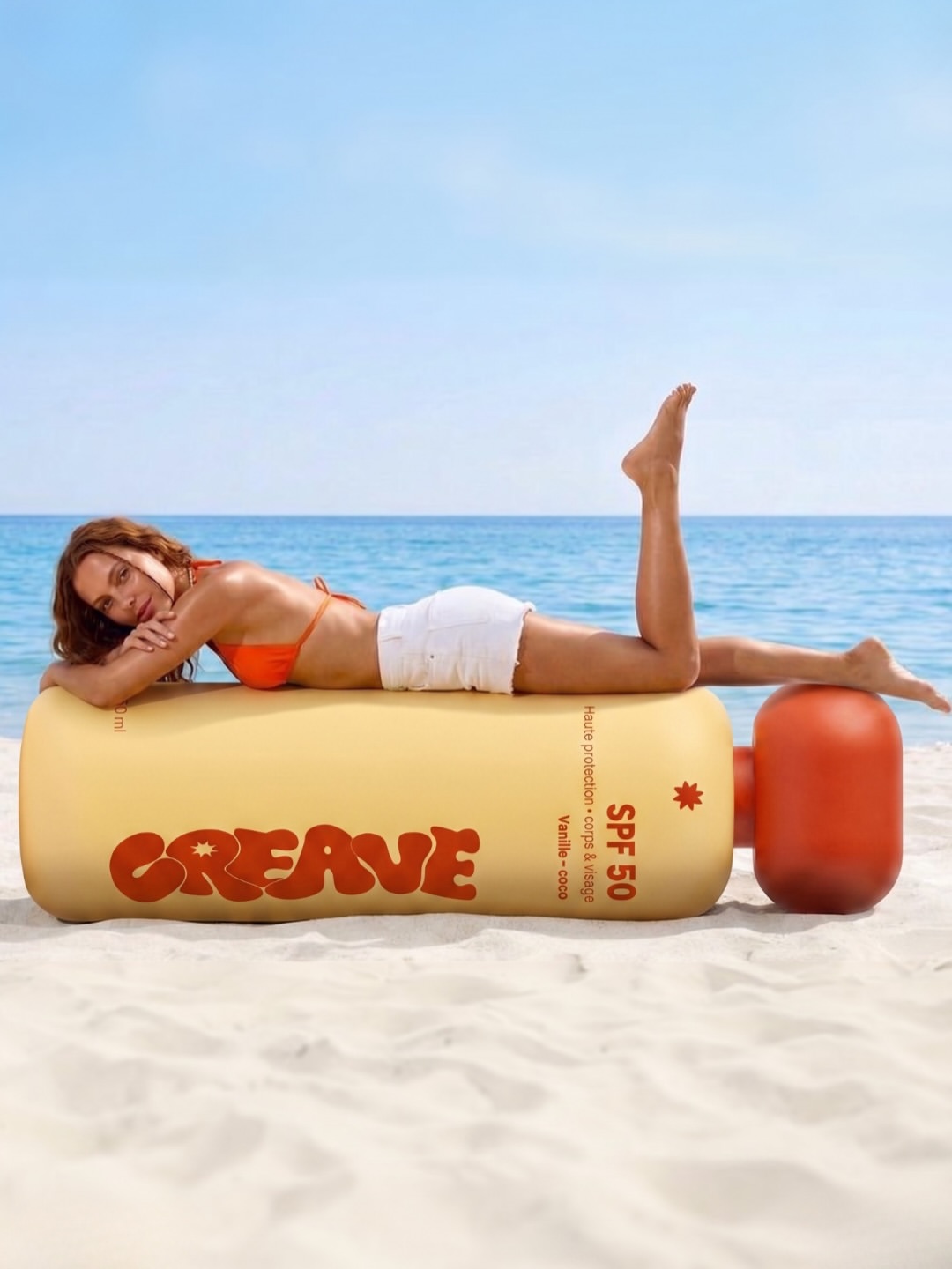 Flacon CREAVE géant gonflable sur une plage, une femme allongée dessus