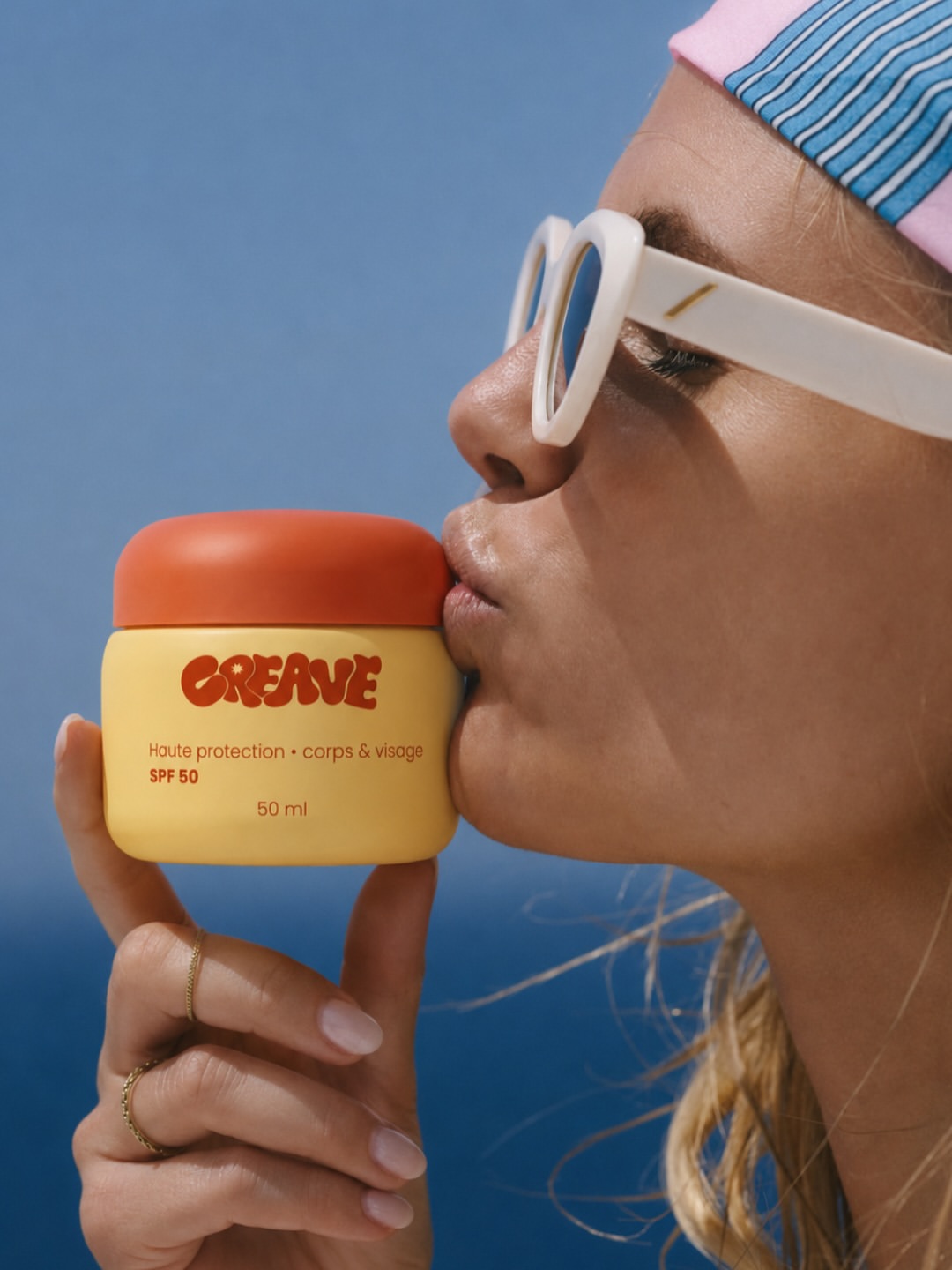 Femme embrassant le pot de crème visage CREAVE SPF 50 sur fond bleu