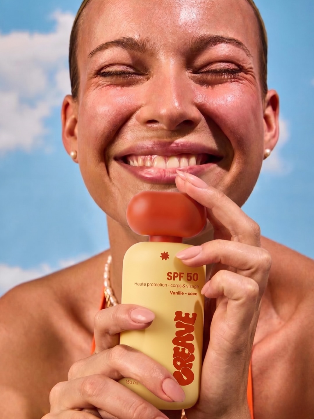 Femme souriante tenant le flacon CREAVE SPF 50 devant un ciel nuageux